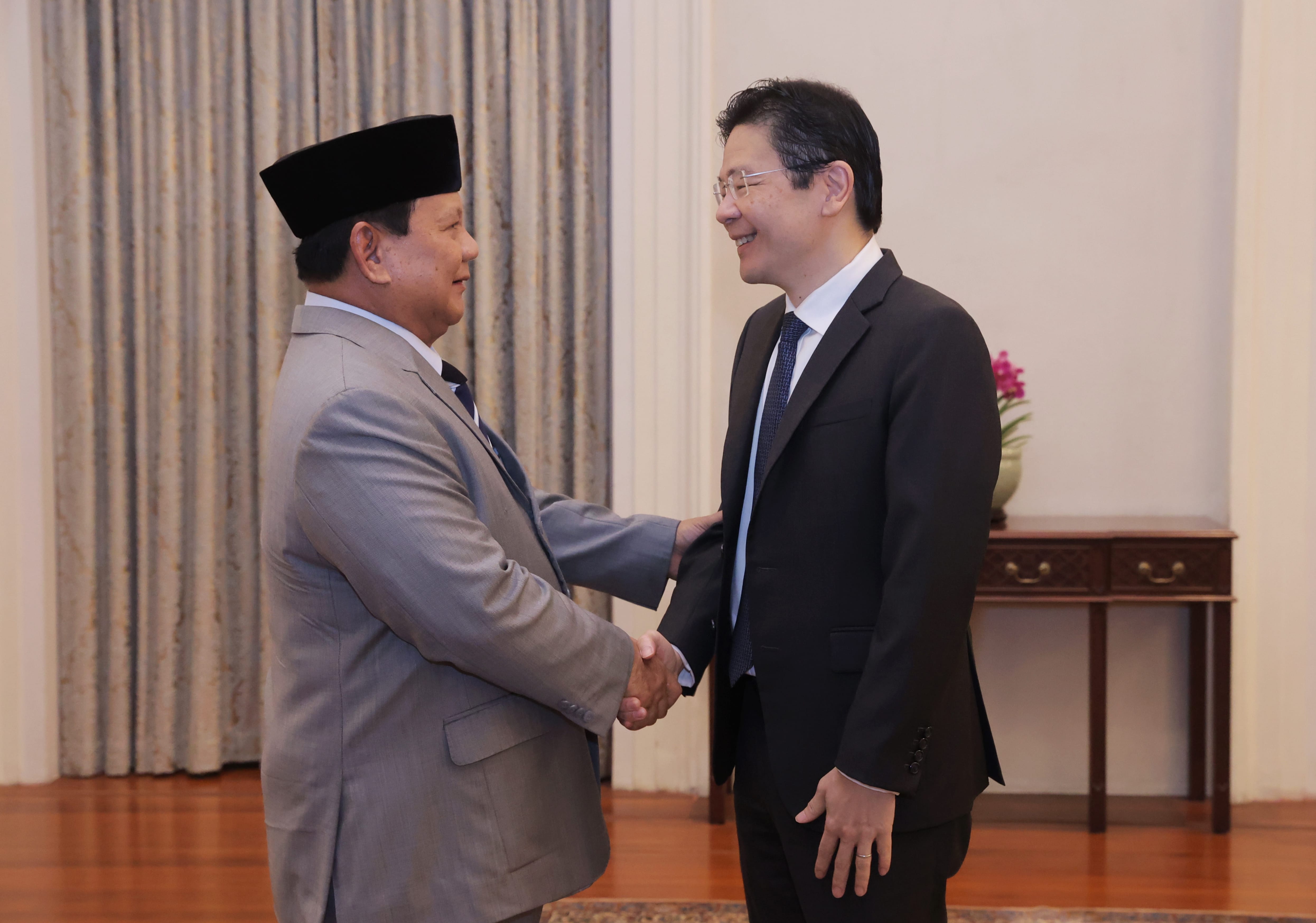 Two men in suits shaking hands, one wearing a peci hat.